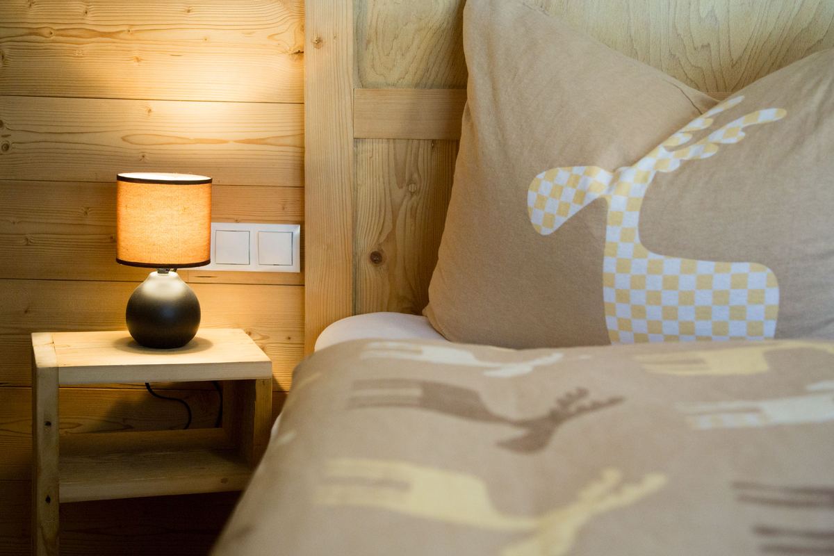 Bettdetail mit Nachttischlampe und Kissen mit Hirschmotiv