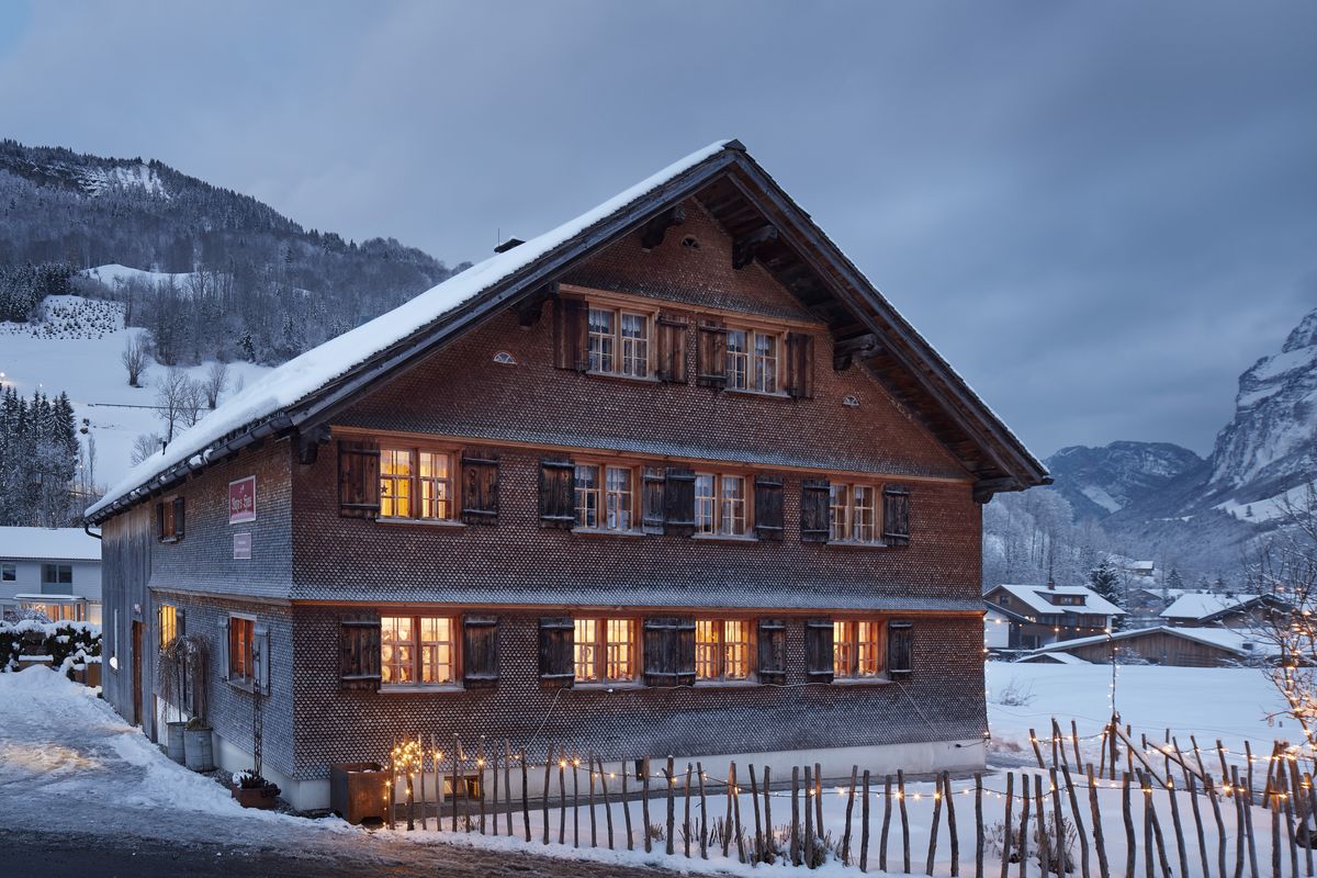 Traditionelles Bregenzerwälder Gasthaus mit warm erleuchteten Fenstern in der winterlichen Dämmerung