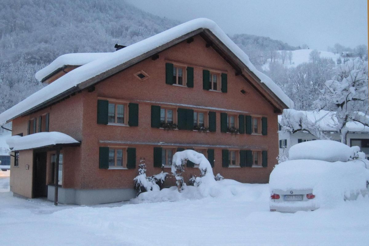 Das Haus Appartement Moosmann in Mellau mit rotbrauner Holzfassade unter tiefem Schnee