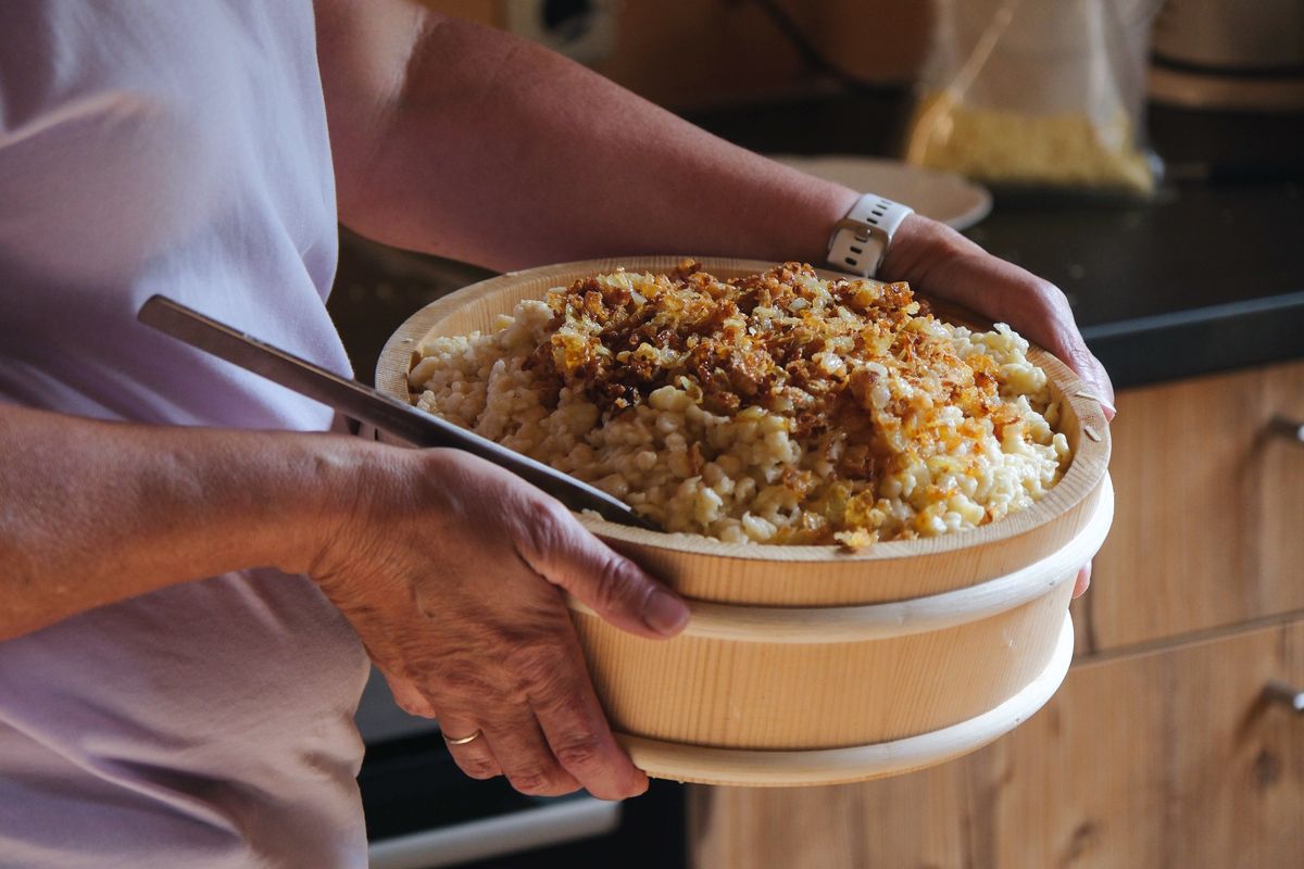 Eine Schüssel frisch gemachter Bregenzerwälder Käsknöpfle mit gerösteten Zwiebeln wird aus der Küche getragen