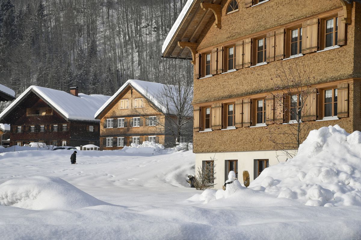 Bregenzerwälder Holzhäuser mit Schindelfassaden im tiefen Schnee, dahinter der bewaldete Hang