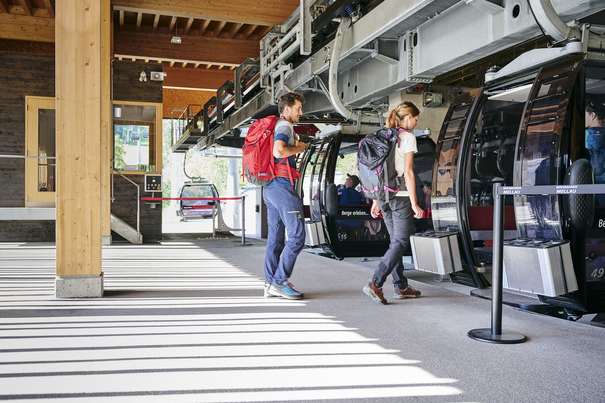 Zwei Gäste mit Rucksack steigen im Sommer an der Talstation in die Gondel der Mellaubahn