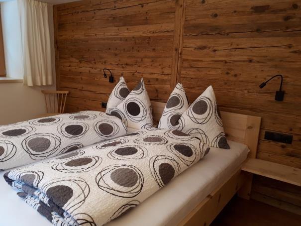 Detail des Bettes: gemusterte Kissen und Bettwäsche vor der Altholzwand