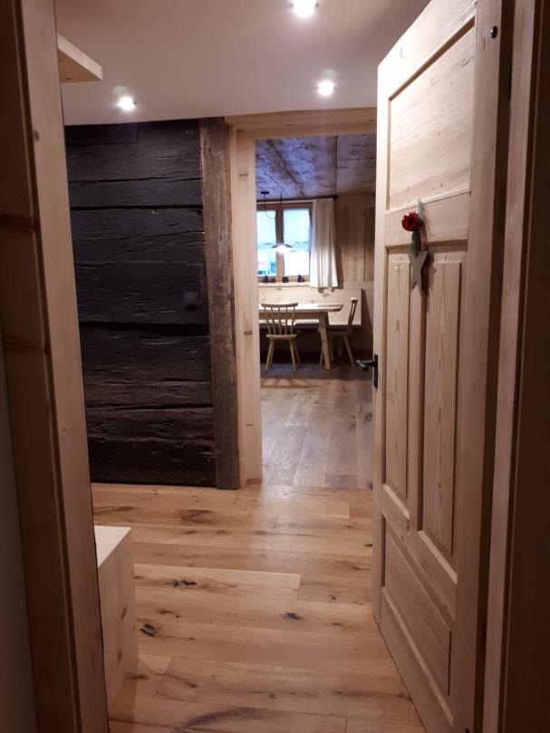 Blick durch den Flur mit dunkler Altholzwand in den hellen Essbereich