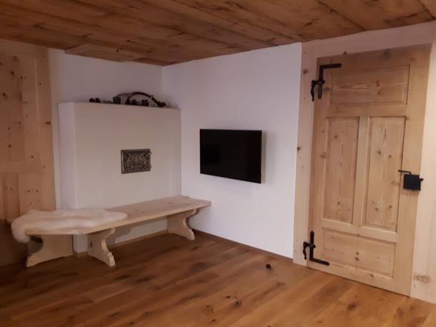 Fernseher an der weißen Wand über einer geschwungenen Sitzbank aus Altholz
