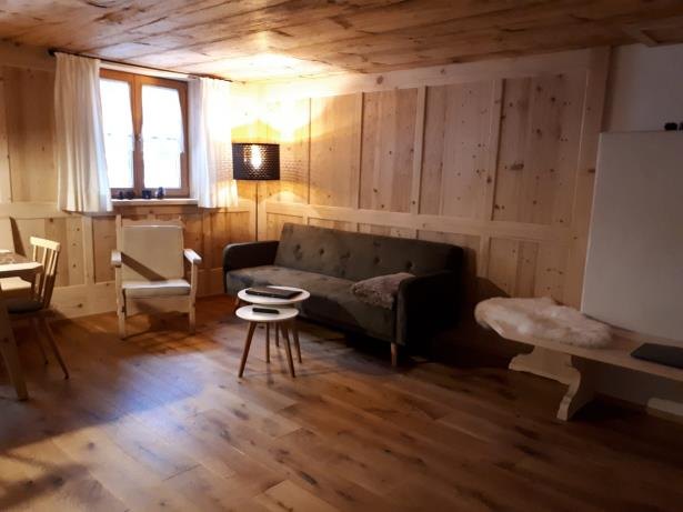 Sofa und Sitzbank aus Altholz im Wohnraum, daneben zwei Fenster mit hellen Vorhängen