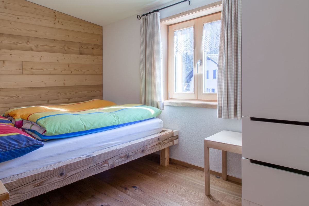 Schlafzimmer mit Holzbett und Fenster zum Dorf