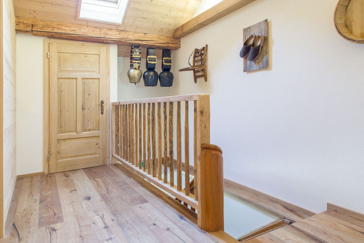 Treppenhaus mit alter Holztür, Geländer und abgestellten Skischuhen