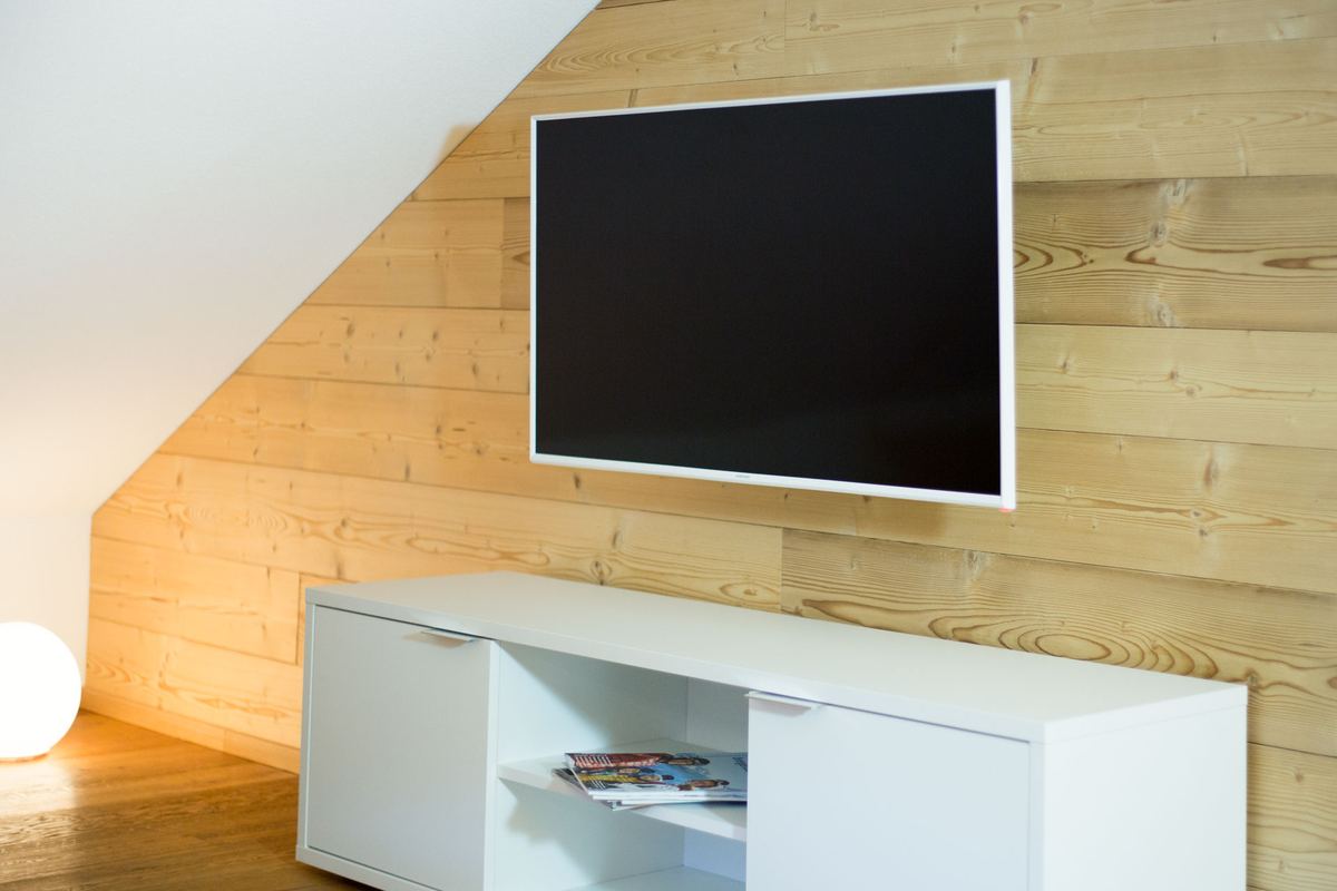 Fernseher an der Altholzwand über einem weißen Sideboard