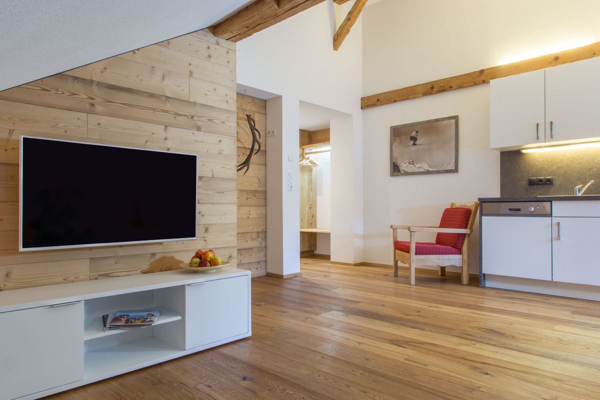 Wohnzimmer mit Fernseher an einer Wand aus altem Holz und Blick zur offenen Küche